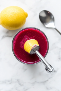 This image shows a juicy lemon being squeezed by hand into a deep red beetroot juice blend, with droplets mid-air and a citrusy freshness captured perfectly