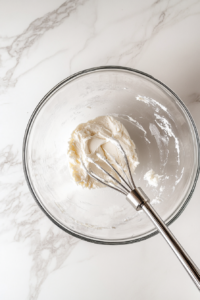 This image shows cream cheese being mashed in a bowl until it becomes smooth and creamy.
