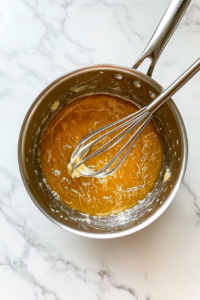This image shows butter melting and sugar dissolving in a medium saucepan to form the base for brownie batter.