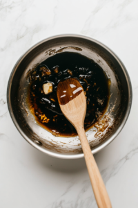 This image shows butter, sugar, and syrups melting together in a saucepan, forming a rich, sticky, and caramel-like base for the Parkin mixture.