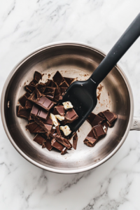 This image shows white chocolate being melted in a bowl placed over simmering water, becoming glossy and smooth as it softens.
