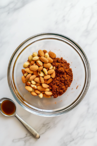 This image shows a variety of nuts, including almonds, being tossed with a touch of seasoning in preparation for roasting.