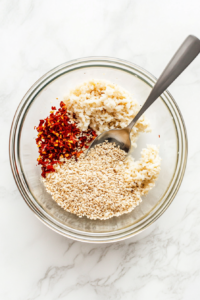 This image shows a small bowl filled with a creamy, green Asian avocado dressing being stirred until smooth and well combined.