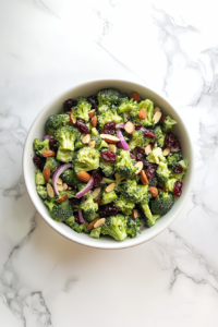 This image shows all the ingredients—broccoli, onions, cranberries, dressing, and roasted nuts—being gently combined into a creamy, colorful salad.