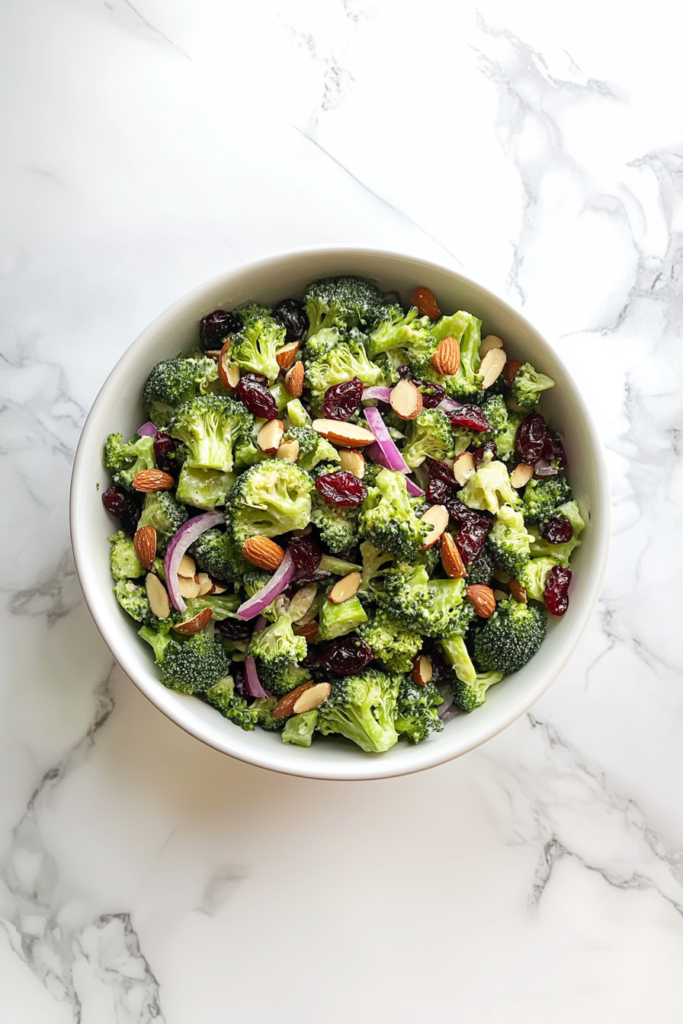 This image shows all the ingredients—broccoli, onions, cranberries, dressing, and roasted nuts—being gently combined into a creamy, colorful salad.