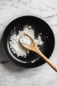 preparing-flour-mixture-in-black-skillet-over-marble-surface