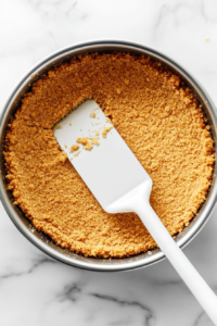 This image shows the graham cracker crust being firmly pressed into the bottom of a 9-inch springform pan.