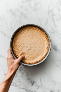 pressing-the-crumbled-crackers-mixture-in-the-baking-pan-for-proper-layering-of-cheesecake