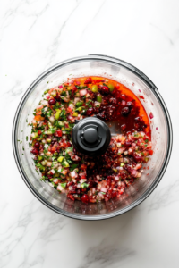 This image shows the cranberry jalapeño mixture pulsed until finely chopped inside the food processor, creating a colorful and textured blend.