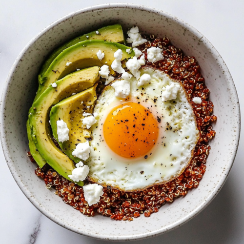 This image shows a white ceramic bowl filled with fluffy quinoa, perfectly cooked eggs, and creamy avocado slices, artfully arranged for a wholesome and satisfying breakfast bowl.