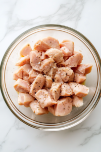 raw-chopped-chicken-seasoned-in-clear-glass-bowl-on-white-marble