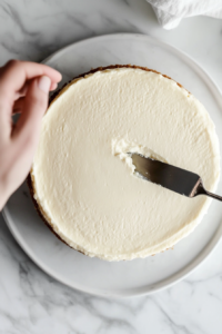 This image shows a hand gently releasing the latch of a springform pan and placing the cheesecake onto a serving plate.