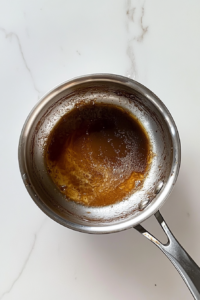 This image shows a hand taking the saucepan off the heat after the sugar has fully dissolved into the melted butter.