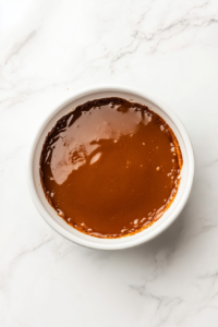 This image shows a round white bowl with rum glaze to coat the golden brown butter rum pound cake generously covering the top and sides, resting on a white marble cooktop.