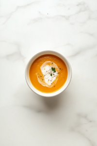 This image shows the finished butternut squash soup served hot in a white bowl on a white marble countertop.