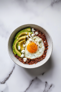 This image shows luscious avocado slices and crumbled feta cheese artfully arranged atop the quinoa and eggs, ready to be enjoyed.