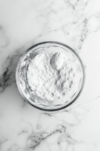 small-clear-bowl-filled-with-powdered-sugar-on-white-marble