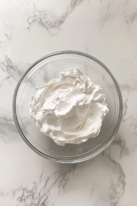 This image shows a bowl of smooth white glaze made from powdered sugar, milk, and vanilla extract on a marble counter.