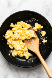 This image shows scrambled eggs being gently cooked in a pan, fluffy and golden as they begin to set into soft curds.