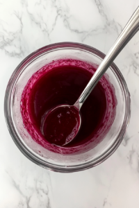 This image shows a spoon gently stirring freshly made beetroot juice in a clear glass pitcher, with the rich red color swirling beautifully.