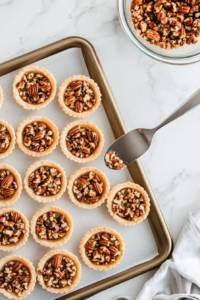 This image shows the pecan pie mixture being carefully spooned into mini pie crusts, each one ready for baking.