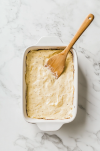 This image shows half of the creamy sour cream mixture being evenly spread across the bottom of a baking dish, forming a velvety base layer.