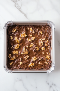 This image shows brownie batter being spread evenly into a lined baking pan, ready for baking.