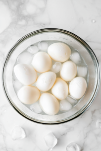 This image shows eggs being chilled in a bowl filled with ice water. The ice cubes glisten as they cool the freshly boiled eggs to stop the cooking.