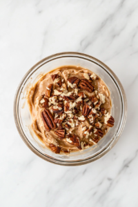 This image shows caramel being stirred together with chopped pecans, forming a sweet and nutty mixture that will go inside the cheese ball.