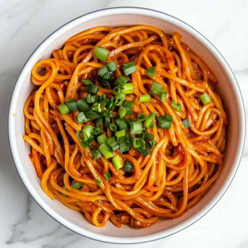 sweet-chili-noodles-in-white-bowl-coated-in-glossy-sauce-with-green-onion-garnish