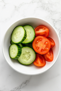 This image shows chunky, peeled cucumber slices added to the bowl alongside the tomatoes to build the fresh salad base.