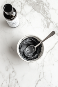 tinting_buttercream_dark_gray_using_black_food_gel_in_glass_bowl_on_white_marble_counter
