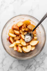 This image shows fresh apple slices being tossed with cinnamon, sugar, and spices to create the sweet base of the apple crisp.