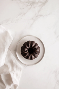 This image shows the fully unmolded chocolate chocolate chip Bundt cake resting on a white ceramic plate over a clean white marble countertop.