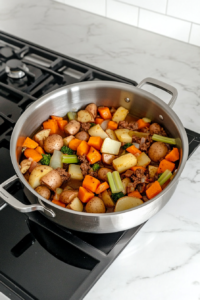 This image shows vegetables including onion, celery, carrot, potatoes, and butternut squash browning lightly in melted butter inside a stainless steel pot placed on a white marble countertop.