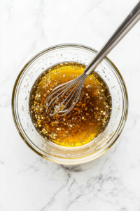 This image shows a creamy dressing being whisked together in a bowl, typically made with mayonnaise, vinegar, and a hint of sugar.