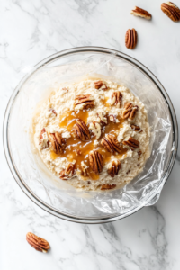 This image shows the cheese ball wrapped in plastic and placed in the refrigerator, allowing it to chill until firm.