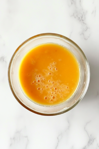 This image shows a top-down view of a glass bowl with flour, baking powder, baking soda, and salt added to the wet mixture on a white marble countertop.
