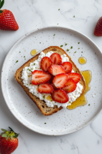 This image shows a top-down view of a slice of toasted multigrain bread on a matte white ceramic plate over a clean white marble countertop, topped with white low-fat cottage cheese, fresh sliced strawberries, and a light drizzle of golden honey.