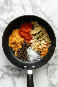 adding-ground-spices-to-sauteed-onion-paste-in-black-skillet-white-marble