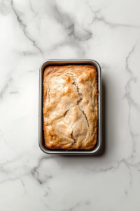 This image shows thick slices of golden-brown banana loaf cake arranged on a round white ceramic plate, placed alone on a clean white marble countertop.