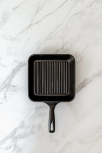 This image shows a black grill pan preheating on a white marble cooktop with a clean and minimal background.