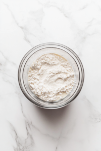 This image shows a glass blender jar filled with smooth crepe batter made from eggs, milk, flour, sugar, salt, and melted butter, placed on a white marble countertop.
