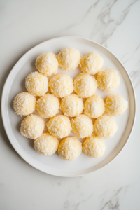 This image shows breadcrumb-coated cheese bites arranged on a white plate over a white marble countertop.