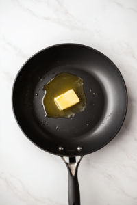 butter-and-olive-oil-melting-in-large-black-skillet-white-marble