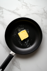 butter-melting-in-black-skillet-with-single-handle-for-keto-butter-chicken-on-white-marble