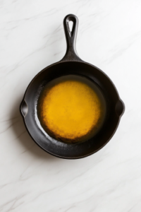 This image shows a large black cast iron skillet filled one-third with vegetable oil, sitting directly on a clean white marble countertop with no other items in the background.