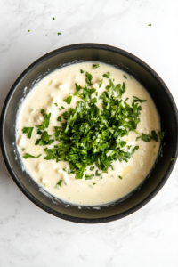 chopped-parsley-stirred-into-garlic-butter-sauce-in-black-skillet-white-marble