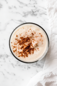 This image shows a glass mixing bowl containing the combined wet and dry ingredients for zucchini banana bread, with a wooden spoon resting beside it on a white marble countertop.