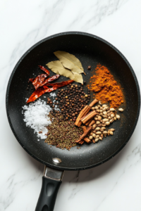 cooking-spices-in-onion-paste-for-flavor-in-black-skillet-white-marble